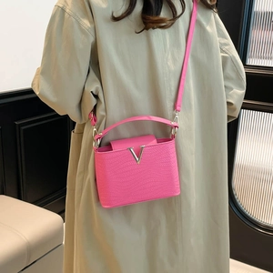 Stijlvolle magenta crossbodytas met golftextuur en zilveren V-gesp op een beige jas