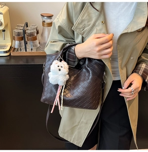 Detail of dark brown woven leather bucket bag with a cute plush dog charm accessory