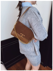 Detailed view of brown leather shoulder bag featuring a gold metal logo and chain strap