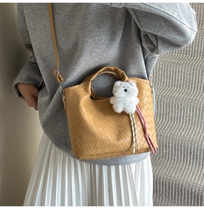Brown woven bucket bag shown on a model with a cute white bear pendant detail