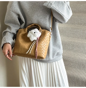 Detailed view of brown woven bucket bag with cute plush puppy charm on a model