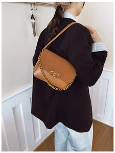 Detail of vintage brown leather handbag with gold chain and metal logo on model