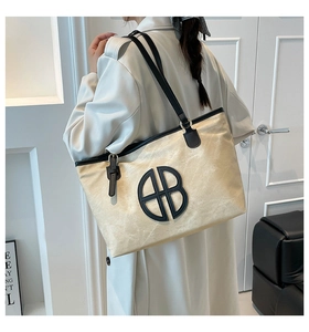 Détail du sac cabas en toile avec garniture en cuir noir et logo rond sur le tissu crème