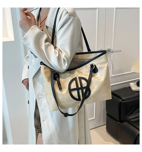 Gros plan d'un grand sac cabas beige avec bordure noire et logo circulaire évidé à l'épaule