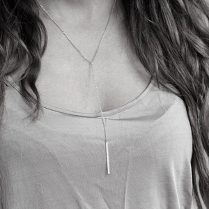 Gros plan du collier lasso en Y argenté minimaliste avec pendentif barre sur le mannequin
