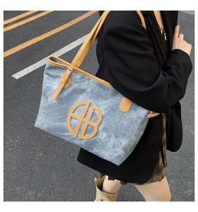 Détail du sac cabas en toile bleue avec lanières en cuir marron et logo découpé dans la rue