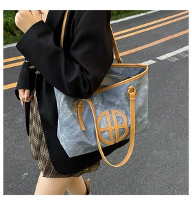 Blue canvas tote bag with leather trim and round logo detail worn by a model