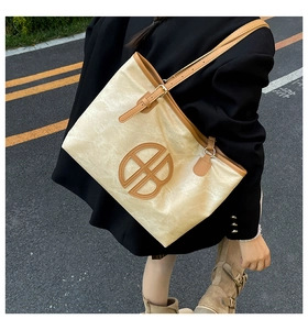 Grand sac cabas beige avec bordures en cuir marron et détail circulaire sur le bitume