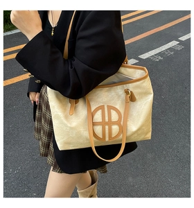 Détail d'un grand sac cabas beige avec garniture en cuir marron et logo circulaire