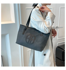Détail du cabas gris foncé avec logo HB circulaire et bandoulière réglable sur le mannequin