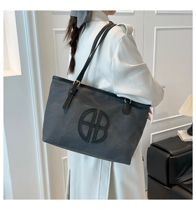 Detail of grey tote bag with circular BB emblem and adjustable black shoulder strap