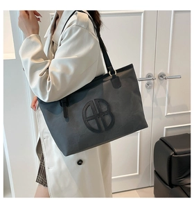 Détail d'un grand sac cabas gris avec logo BB circulaire porté à l'épaule par un mannequin
