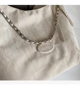 Detail of off-white tote bag with pleated fabric texture and silver chain strap