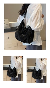 Detail of black pleated tote bag with silver chain and glossy finish on shoulder