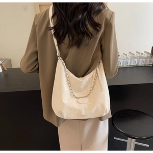 Detail of white tote bag with textured surface, metal chain, and adjustable crossbody strap