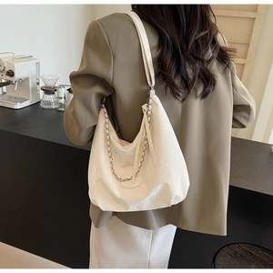Detailed view of white textured tote bag with silver chain on model in cafe setting