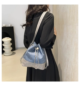 Detail of denim and grey leather bucket bag featuring chain drawstring and slim strap