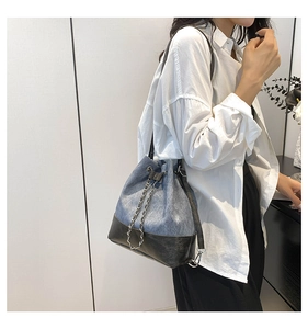 Detail of color-blocked bucket bag with denim texture and metallic chain drawstring