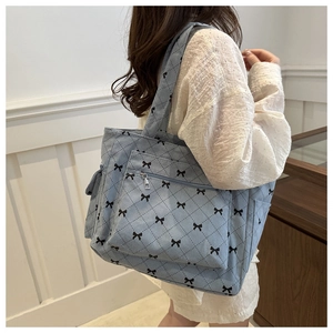 Blue corduroy quilted tote bag with black bow print shown worn on model's shoulder