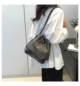 Detail of grey bucket bag with silver chain worn by a model in a minimalist room