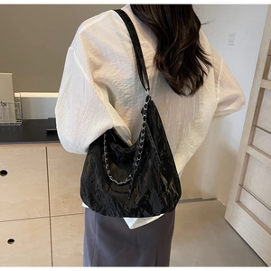 Detail of black pleated hobo bag with silver chain strap shown on a model shoulder