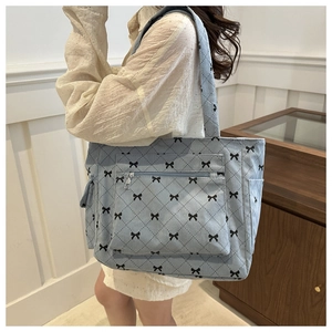 Detail of blue tote bag with bow print, side pocket, and zipper on textured fabric