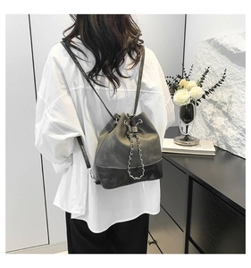 Detail of grey bucket backpack with drawstring closure and decorative metal chains