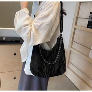 Detail of black pleated PU leather bag with silver metal chain and soft glossy texture