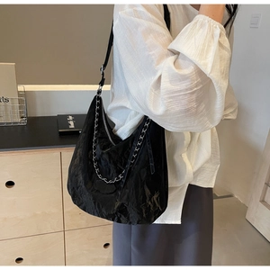 Detailed view of black pleated underarm bag with elegant silver chain and smooth zipper