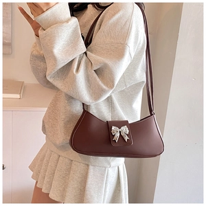 Détail du sac sous le bras en cuir marron foncé avec boucle nœud argentée et bandoulière