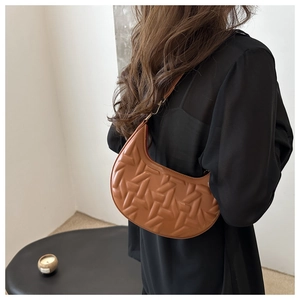 Close-up of brown crescent underarm bag featuring a 3D geometric embossed texture