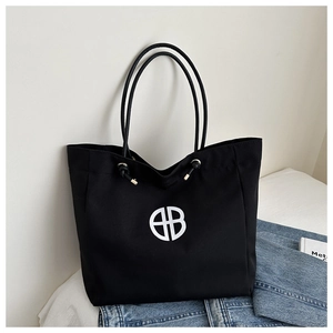 Primer plano del bolso tote de lona negra con logo circular blanco y hebillas de plata fina