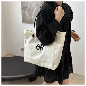 Vista detallada del bolso tote de lona crema con logotipo negro al hombro sobre modelo