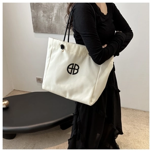 Bolso tote minimalista de lona blanca con logo negro y asas lucido por una modelo