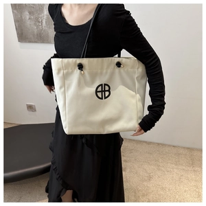 Detalle del bolso tote de lona crema con asas de nudo negro y detalles en metal dorado