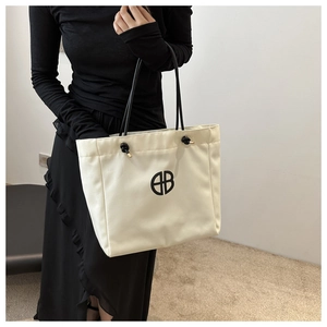 Detalle de un bolso tote de lona beige con asas de cuero negro y diseño de logotipo