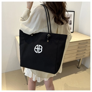 Detalle de un bolso tote de lona negra con logo HB blanco y detalles de ojales metálicos