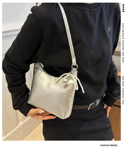 Détail d'un sac à bandoulière argenté avec nœud en perles et pendentif cœur