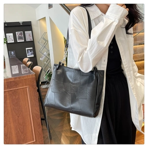 Close-up of black leather tote bag with patchwork design and silver chain shoulder strap