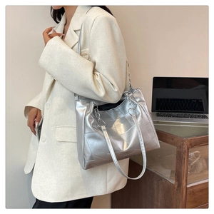 Silver metallic tote bag with geometric patchwork and chain strap shown on model in office