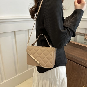 Sac bandoulière beige matelassé avec détails dorés porté par un mannequin en salle