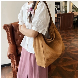 Close-up of a large brown suede hobo bag carried by a model in a warm vintage interior