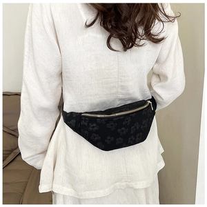 Close-up of black floral jacquard crescent waist bag with metallic zipper and wide strap