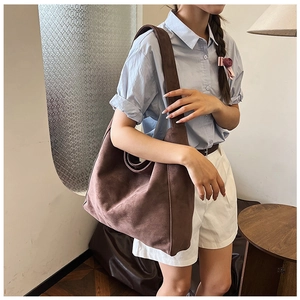 Brown suede tote bag with wide strap worn by a model in a natural light setting