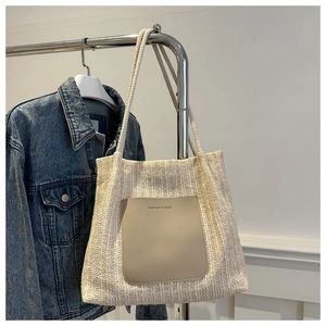 Detail of woven straw tote bag with faux leather pocket hanging next to denim jacket