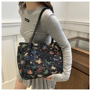 Detail of butterfly embroidery on a black woven tote bag shown on model's shoulder