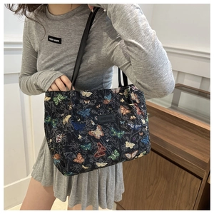 Detail of black tote bag with colorful butterfly jacquard and leather logo plate
