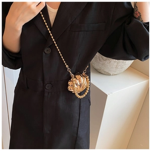 Close-up of golden shell-shaped mini bag with bead chain strap on black dress