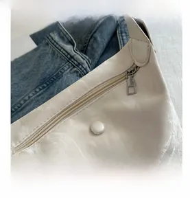 Gros plan sur un sac crème texturé avec fermeture éclair métallique et boucle assortie