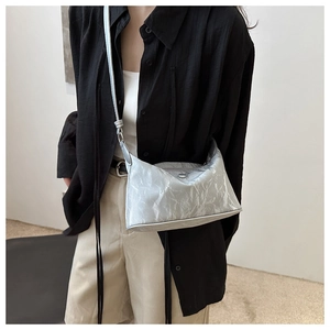 Détail du sac à main argenté en cuir plissé avec plaque logo porté par un modèle